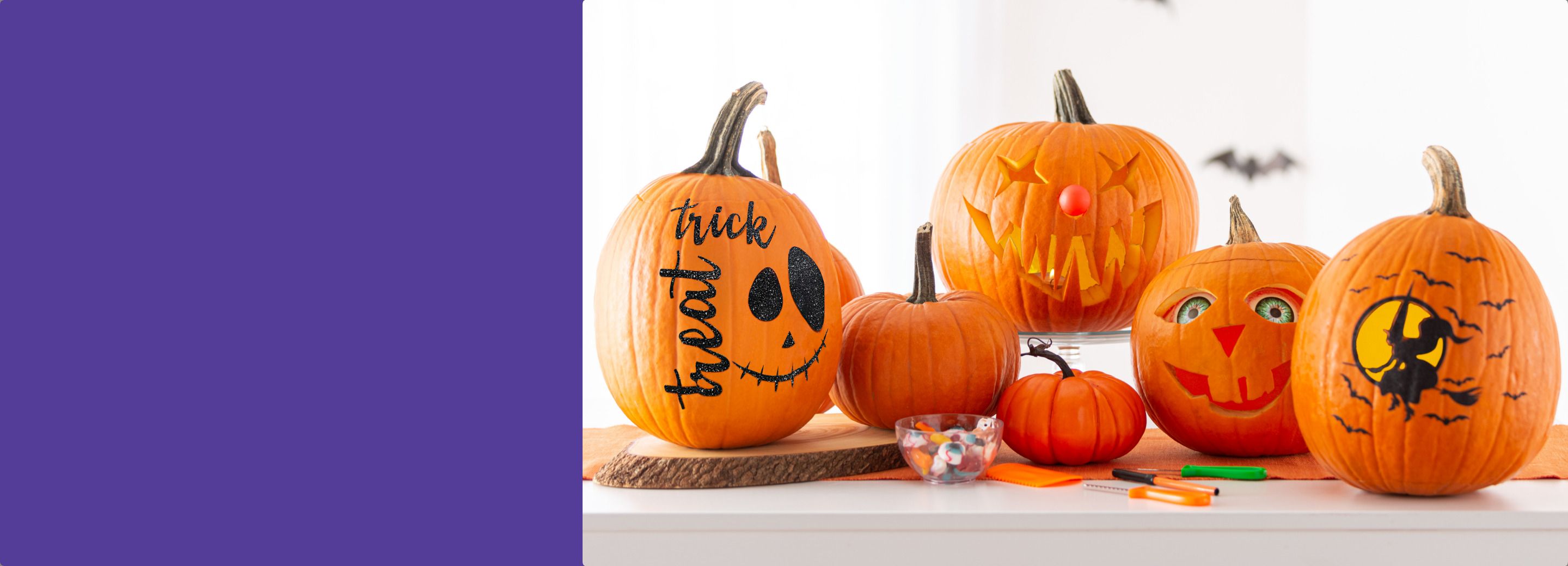 A variety of carved and decorated pumpkins sitting on a countertop with carving tools and a bowl of pumpkin decorating accessories.
