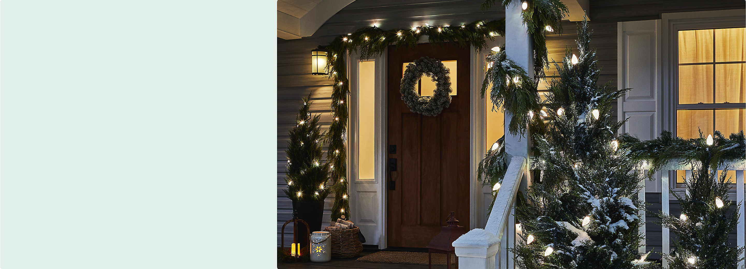 A front porch of a house decorated with white outdoor lights, green Christmas garland and a wreath hung on the front door. 