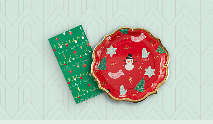 A red Sophistiplate Deck the Halls plate with Christmas-themed print and a Sophistiplate Deck the Halls guest towel with a green print. 
