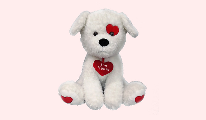 Un chien blanc en peluche avec des cœurs rouges et un cœur autour du cou avec « I’m Yours » écrit en blanc.
