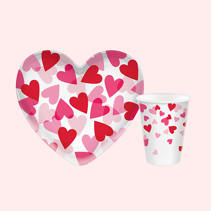 A Valentine&#39;s Day heart-shaped plastic bowl and a matching cup, both white with a red and pink heart print.