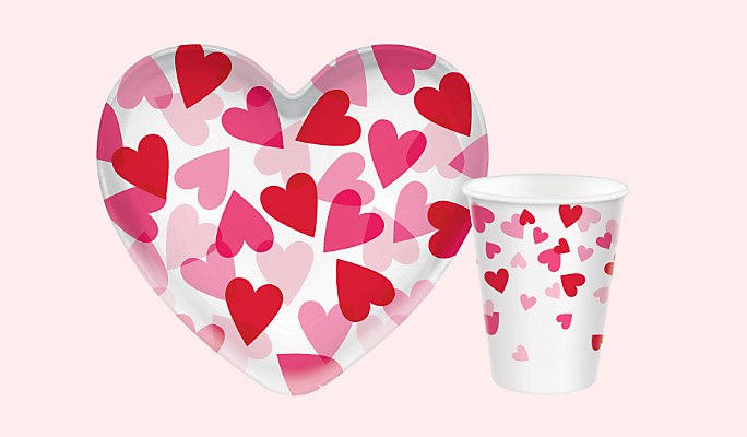 Un bol en plastique en forme de cœur pour la Saint-Valentin et un verre assorti, les deux blancs avec un motif de cœurs rouges et roses.