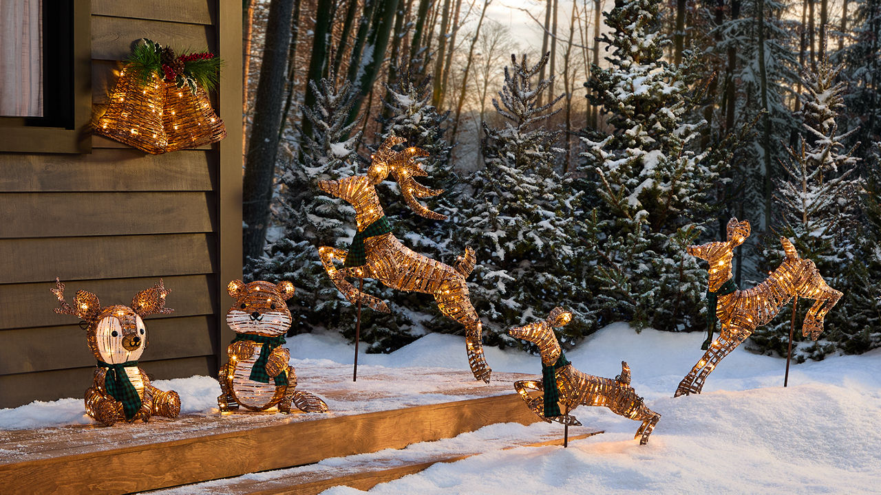 A rustic cabin in the snow with LED bells, a beaver, and deer lawn decorations. 