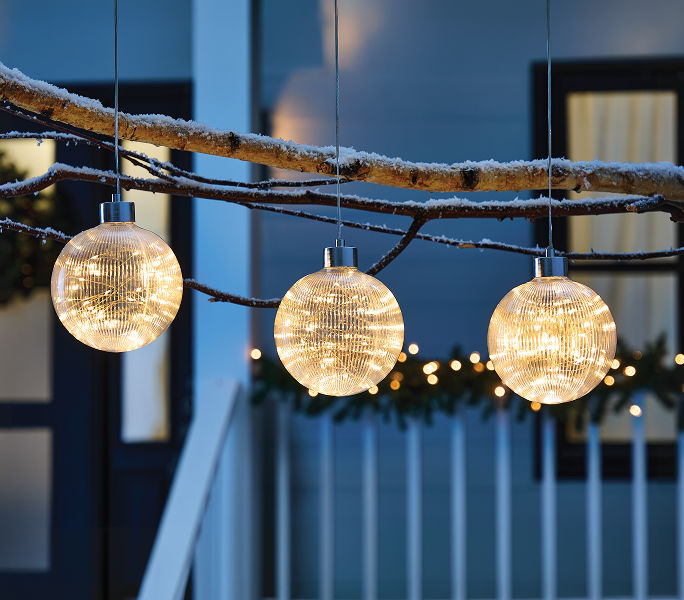 Three illuminated globe lights hanging from snow-covered branches above an outdoor porch.