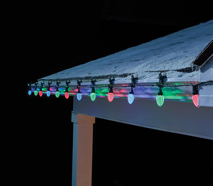 Multicolour C9 Christmas lights installed along a snow-covered roofline on a home exterior.