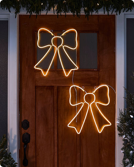 Two illuminated bow decorations mounted on a front door and glowing with warm white light.