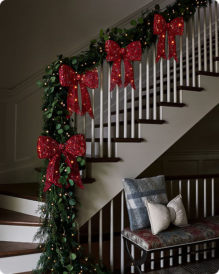 Decorative staircase garland adorned with large red illuminated bows and holiday greenery.
