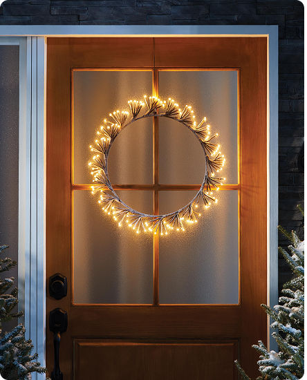 Lit Christmas wreath hanging on a front door and wrapped with warm white LED lights.