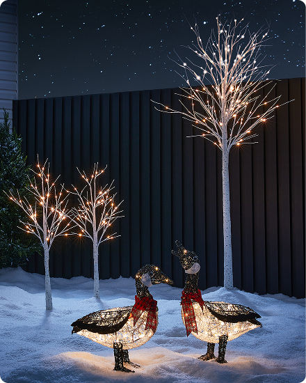 Illuminated decorative trees and light-up bird figures displayed in a snowy outdoor setting at night.