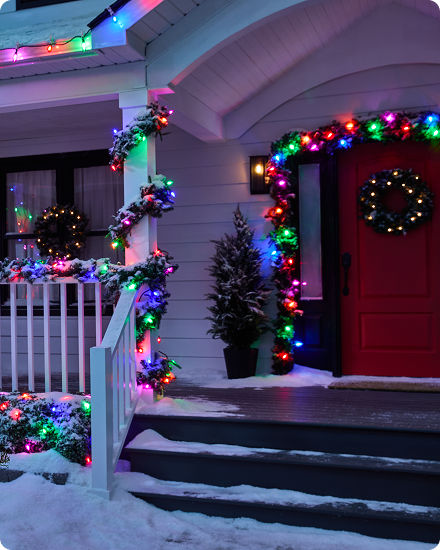 A front porch decorated with oversized multi-colour Christmas lights wrapped around railings, garland and exterior trim.