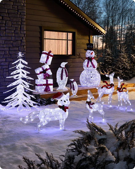 An outdoor holiday display featuring illuminated white deer, snowmen and decorative trees in a snowy yard.