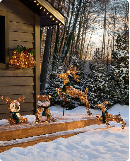 A snowy cabin in the woods decorated with various LED deer, a beaver and Christmas bells. 