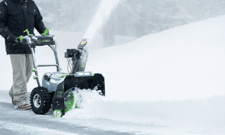 EGO. Snow blower clearing a snow-covered driveway, ejecting snow through the discharge chute.