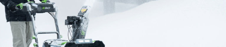 EGO. Snow blower clearing a snow-covered driveway, ejecting snow through the discharge chute.