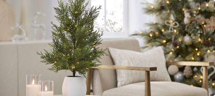 White birch-style tabletop tree featuring illuminated branches, displayed among frosted greenery and pinecones in a softly styled holiday vignette.