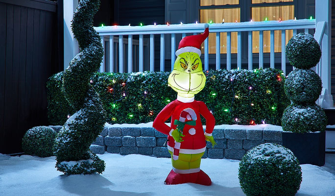 An Airblown Grinch inflatable holiday decoration holding a candy cane on a snow-covered lawn.