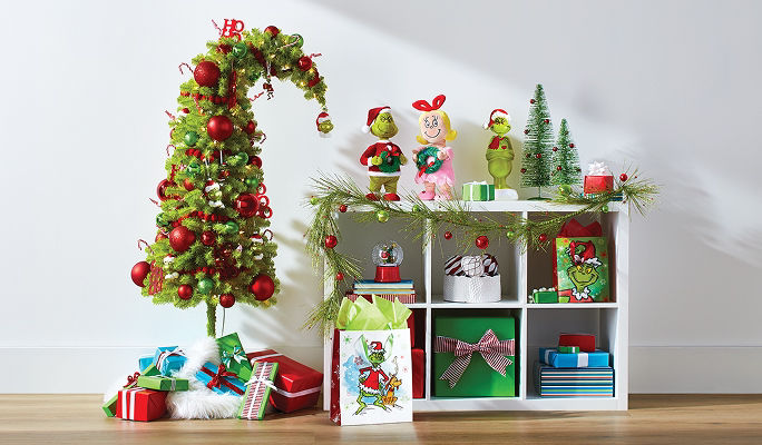 A Grinch-inspired For Living Crumpit Christmas tree displayed beside holiday figurines, wrapped gifts and seasonal decor.