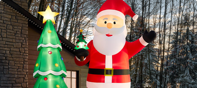 Large outdoor inflatable Santa Claus standing beside a decorated Christmas tree in a snowy yard, promoting Christmas decorations, trees and festive decor..