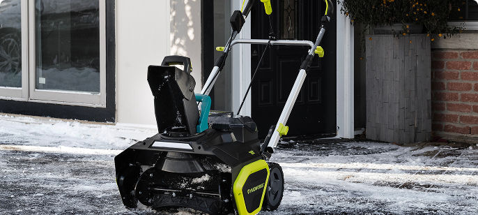 Electric snow blower clearing snow from a residential driveway, promoting snow removal equipment for winter weather preparation.